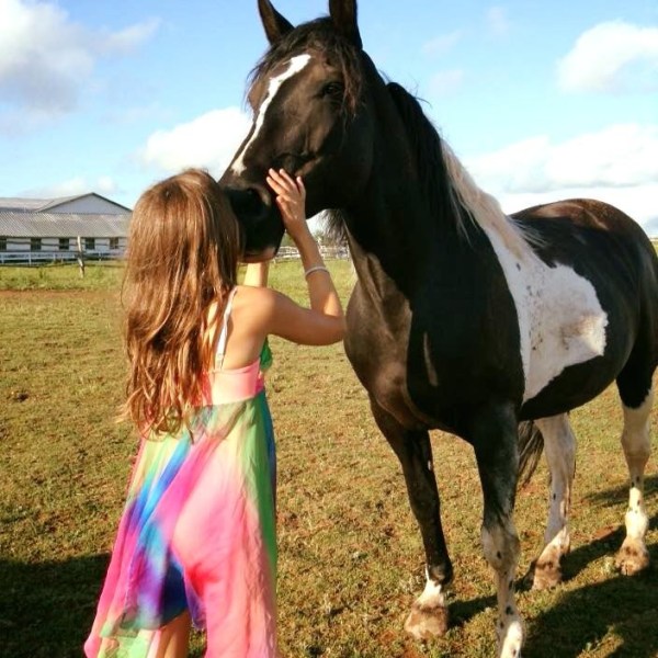 a little girl standing next to a horse