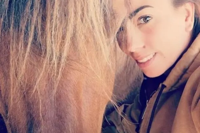 Person smiling next to a horse in a stable.