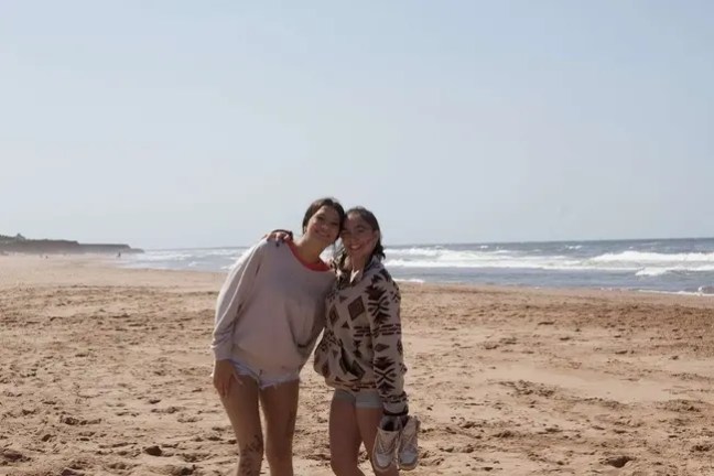 Two people standing on a beach with the ocean in the background.