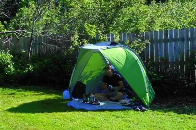 Person sitting in a green tent in a garden with a wooden fence.