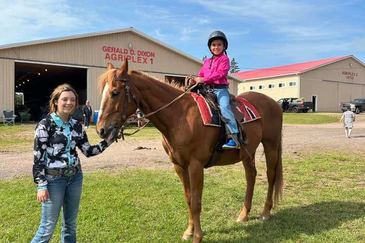 Child riding a horse led by an adult, buildings labeled Agriplex in the background.