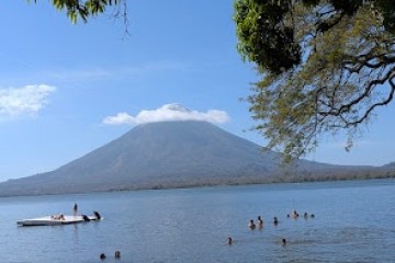 People swimming in a lake with a volcano in the background under a clear blue sky.