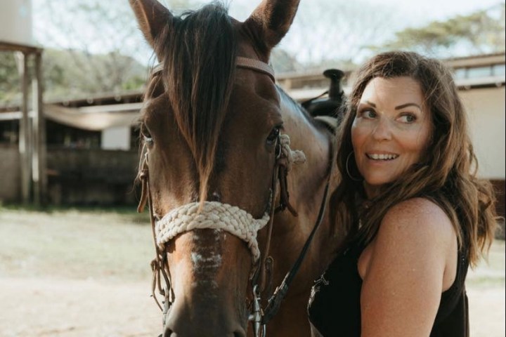 Woman smiling next to a horse in an outdoor setting.